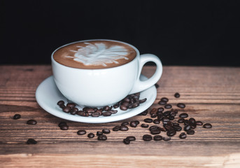 A cup of cappuccino coffee and freshly roasted coffee beans on a rustic wooden table with blank space for your text.