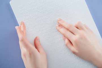 partial view of young woman reading braille text with hand isolated on violet