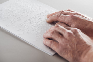 cropped view of senior man reading braille text isolated on grey