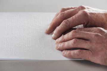 partial view of senior man reading braille text isolated on grey - obrazy, fototapety, plakaty
