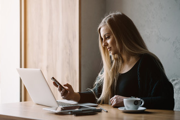 Beautiful girl working out a plan of the project and concept. Girl paints a website design on a laptop. student prints a message on the phone in the messenger. Development. Digital marketing