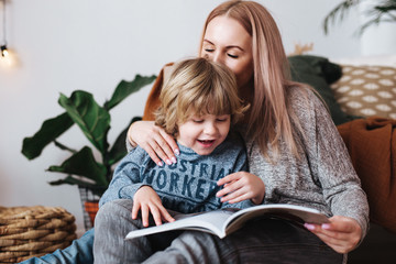 Mother and little son sitting and reading book together at home