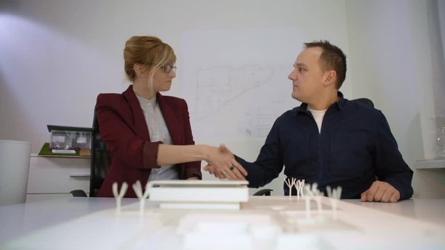 Two architects handshaking behind a model house in office