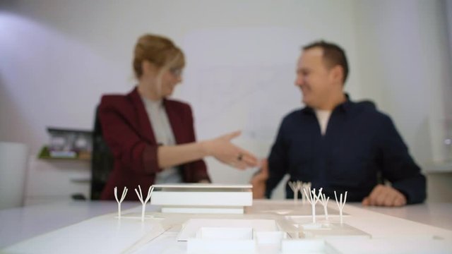 Two architects handshaking behind a model house in office