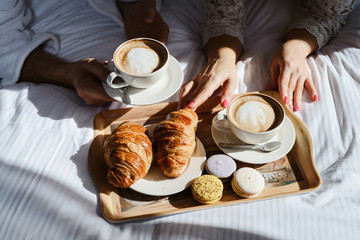 Breakfast in bed. Window light. Two cups of coffee for couple, croissants, butter and sweets