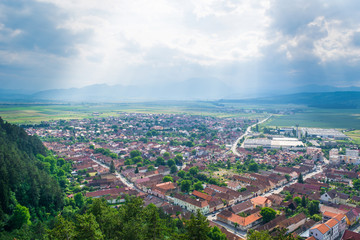 Traditional and historic Rasnov city center panorama on a sunny summer day in Transylvania, Romania, Eastern Europe. Medieval buildings, mountains  and green fields. Famous travel destination. 
