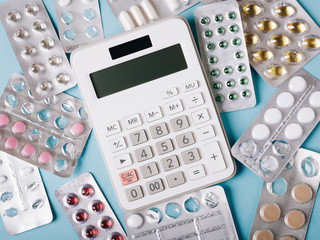White calculator and pills on a blue background as a symbol of paid (expensive) medicine