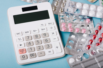 White calculator and pills on a blue background as a symbol of paid (expensive) medicine