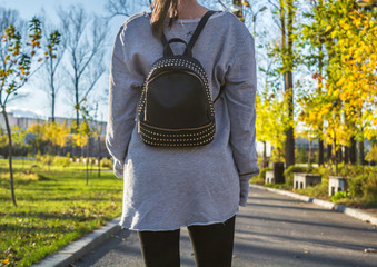 Young girl wearing gray sweatshirt and black yoga pants walking in the park. Black backpack with rhinestones as accessory. Casual style.