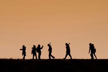 Silhouettes of hikers with backpacks enjoying sunset view from top of a mountain