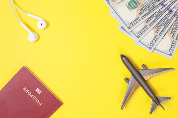 One hundred dollar bills, airplane, headphones, foreign passport on bright yellow paper background. Copy space. Travel and low budget trip concept, flat lay. Top view. Frame of objects