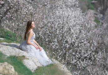 Fototapeta na wymiar Beautiful girl in a blooming spring garden. She's wearing a wedding dress