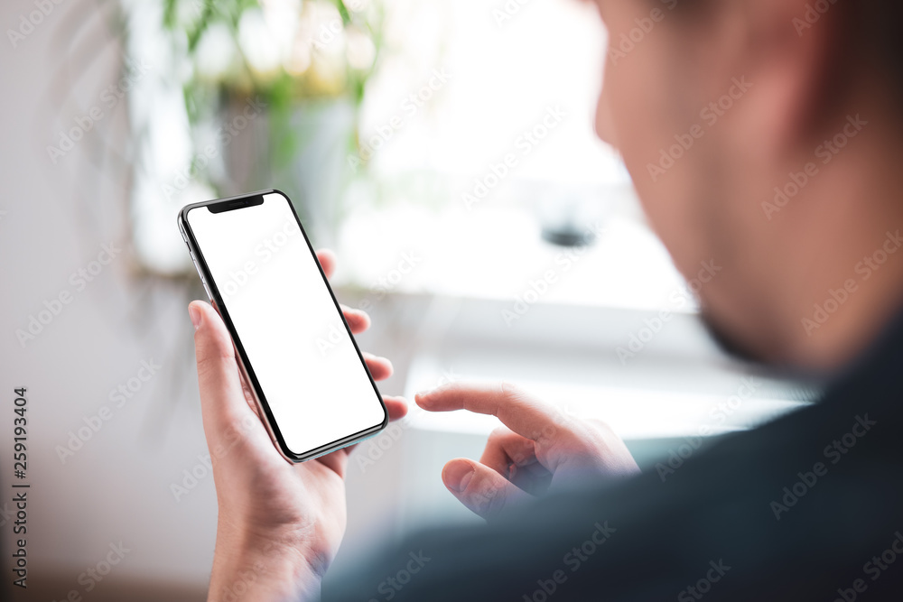 Poster man hand holding the black smartphone with big blank screen and modern frame less design in home int