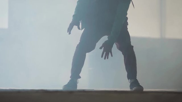 Experienced young hip-hop street dancer performing in front of large window in the dark abandoned building. Contemporary. Hip hop culture. Rehearsal. Slow motion.