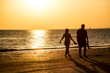 Silhouettes of people on an orange beach at sunset.