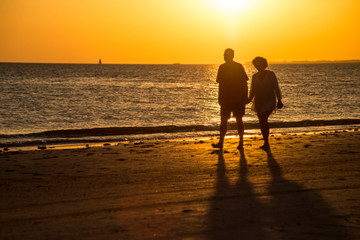 Silhouettes of people on an orange beach at sunset.