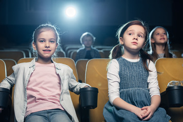 cute children sitting in cinema together with friends and watching movie