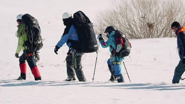 In one line there is a group of well-trained climbers, they rely on the ski poles and make efforts not to fall into the snow moving forward