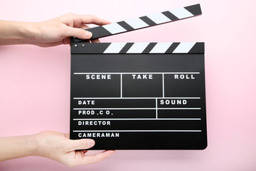 Female hands holding clapper board on pink background