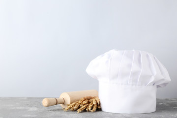 Fototapeta na wymiar Chef hat with rolling pin and wheat ears on grey wooden table