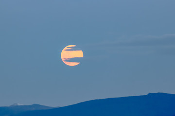 A super moon rises amid the clouds during sunset