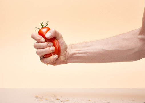 Man's hand crushing tomato against cream background