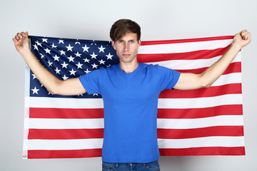 Beautiful young man holding an American flag on grey background