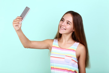 Naklejka premium Beautiful girl making selfie on smartphone on mint background