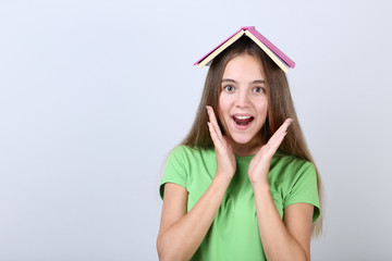 Young girl holding book on her head on grey background