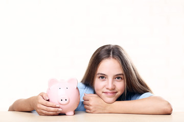 Young girl with pink piggybank sitting at table