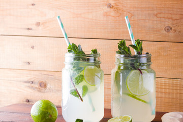 Mojito and mint on wooden background. Refreshing cocktail with lime and fresh mint on wooden boards. Two jars with handles with a summer drink with citrus and ice. Homemade mojito