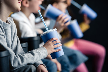 selective focus of friends watching movie in cinema and holding paper cups