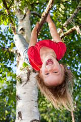 Happy littlr girl hanging from a tree in a summer garden