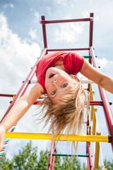 Little girl hanging from a jungle gym playing in a summer garden - child risky play concept
