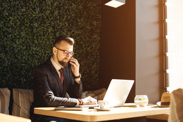 Young businessman working on a plan of Internet project on the laptop. Man discusses business matters by phone. Working computer for internet research. Digital marketing. Development