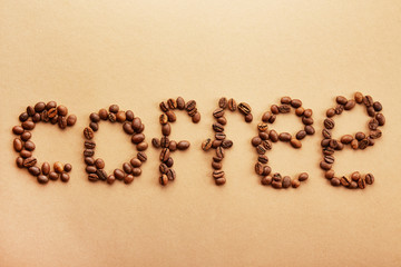 Word coffee spelled with roasted beans over creamy brown background. Close up, copy space, top...
