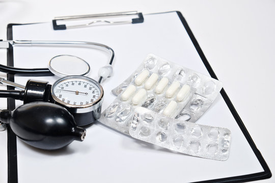 phonendoscope and tonometer  with a folder with white sheets of paper and pills  on a white background
