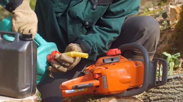un bucheron verse du carburant dans le r&eacute;servoir de sa tron&ccedil;onneuse 