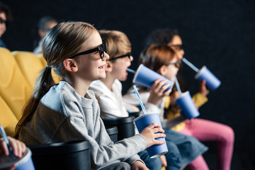 selective focus of multicultural friend sitting in cinema with paper cups and watching movie