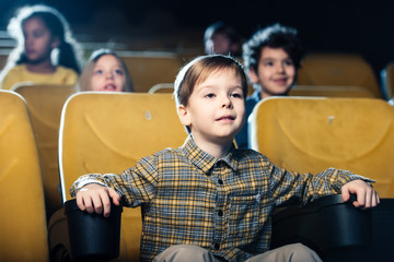 concentrated boy watching movie in cinema together with multicultural friends