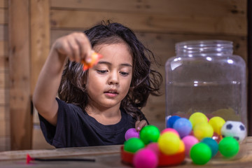 Fototapeta na wymiar a long hair boy wear black shirt playing with colorful balls in wooden room