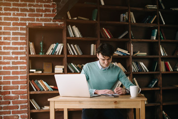 Young handsome student typing on his notebook his diploma. Student discussing on the phone universities's timetable. Education online. Work on freelance. Software development.