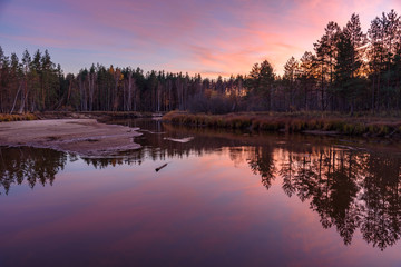 Purple sunset over the forest by the river. Reflection in water. Calm on the river in the forest.