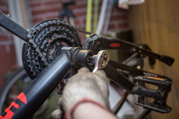 A close-up of a male bicycle mechanic's hand in the workshop uses a screwdriver tool to adjust and repair the bicycle crank assembly, the front bike stars