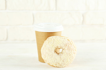 Vibrant composition of lush donut with colorful sprinkled icing and disposable paper cup on wood textured background copy space for text. Tasty but unhealthy food concept. Close up, flat lay, top view