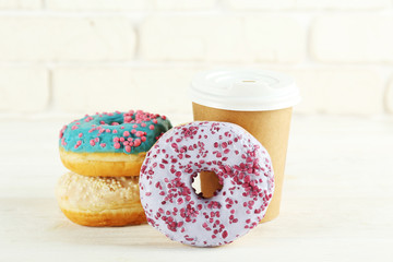 Vibrant composition of lush donut with colorful sprinkled icing and disposable paper cup on wood textured background copy space for text. Tasty but unhealthy food concept. Close up, flat lay, top view