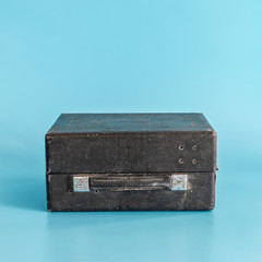 Old black shabby closed suitcase on blue background.  Minimal concept.