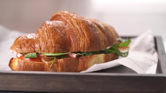 A delicious croissant with ham, cheese and vegetables twisting on a tray.