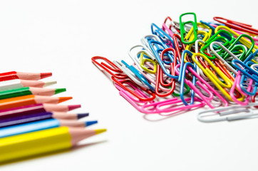 Many multi-colored stationery clips for documents and multi-colored pencils lie on a white background