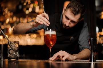 Male bartender pouring red cocktail in glass